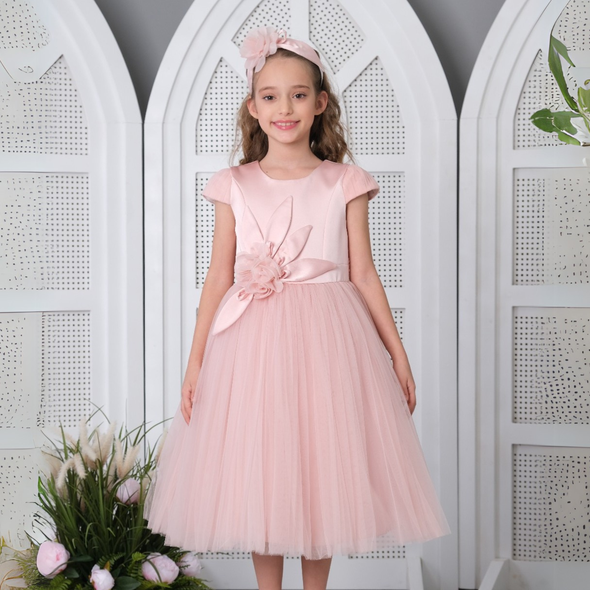 Jeune fille portant une robe rose clair avec une jupe en tulle et un gros détail de fleur, assortie à un bandeau rose