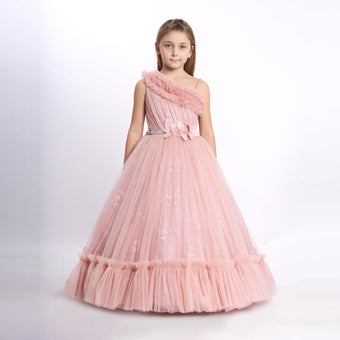 Girl in a floor-length pink tulle ball gown with one-shoulder ruffle detail and floral waist accent, styled for parties or formal occasions.