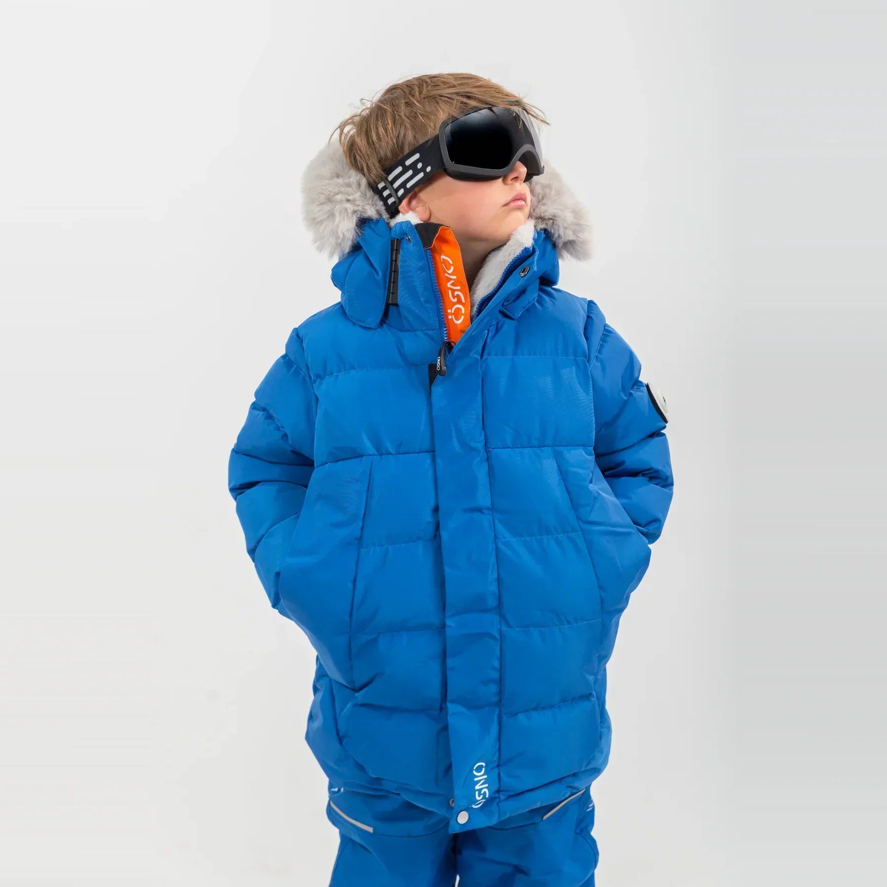 Boy wearing blue ÖSNO ski jacket with faux fur hood trim and orange inner lining.