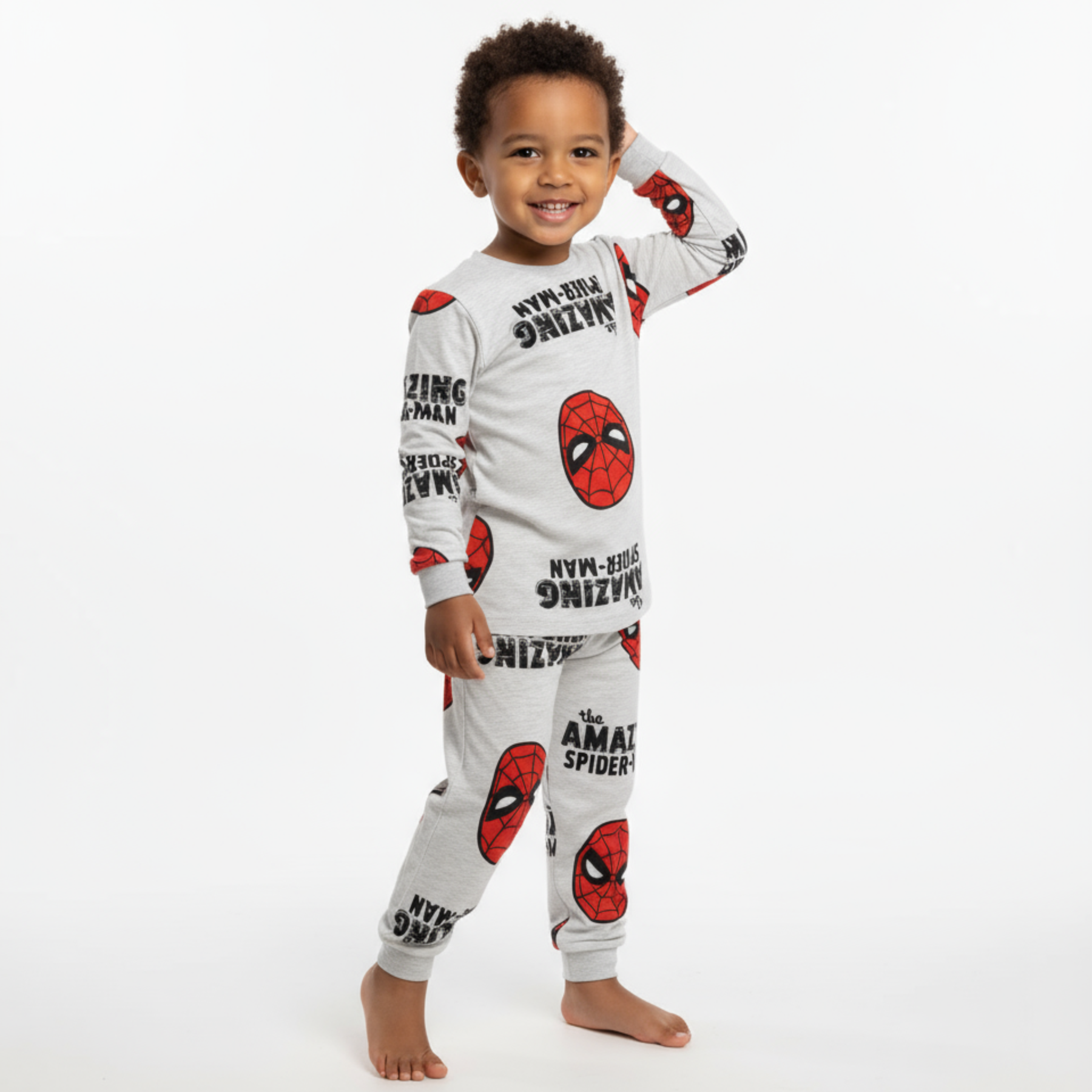 Toddler standing against a white backdrop in grey long-sleeve boys' pyjamas with a red superhero mask print.
