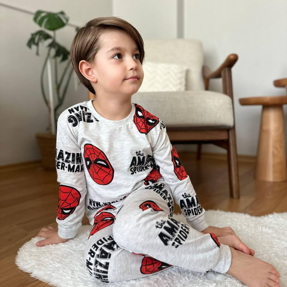 Boy sitting on a white rug in grey long-sleeve boys' pyjamas with an all-over red superhero mask print.