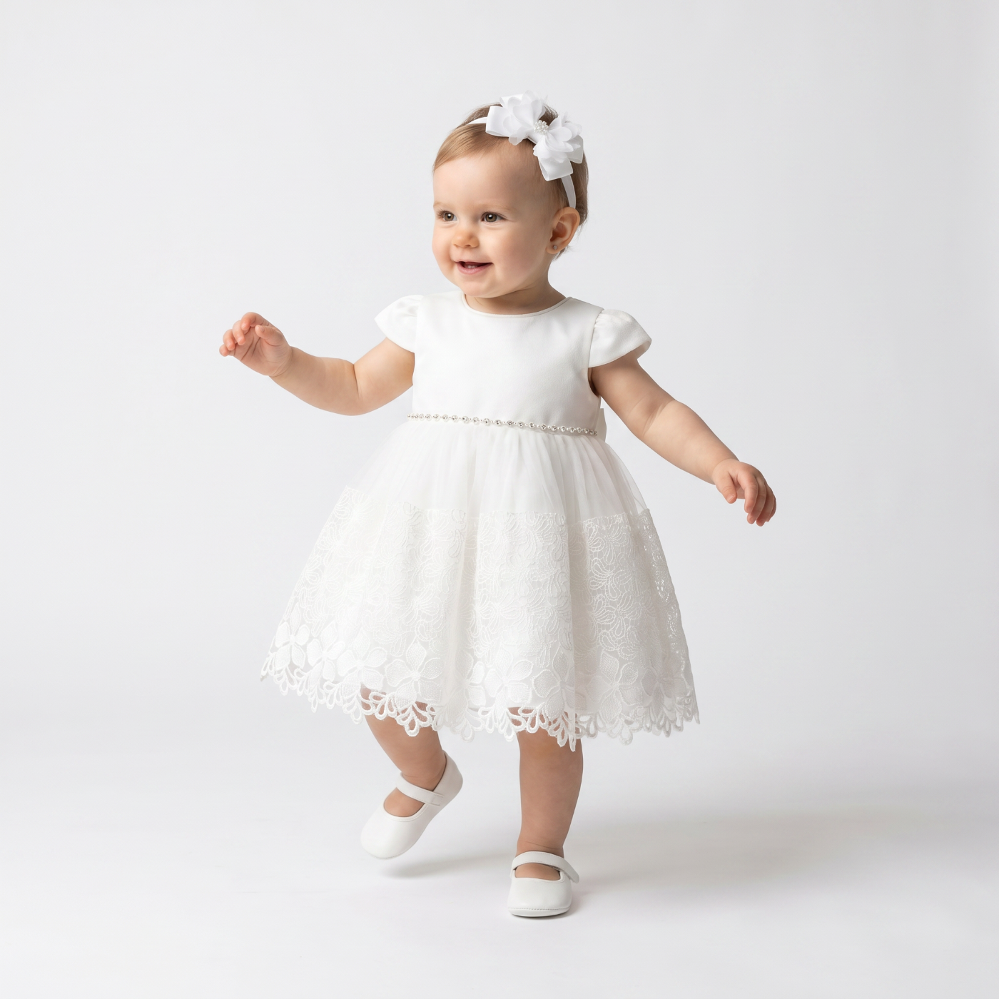 Baby in a white dress with lace details on a plain background