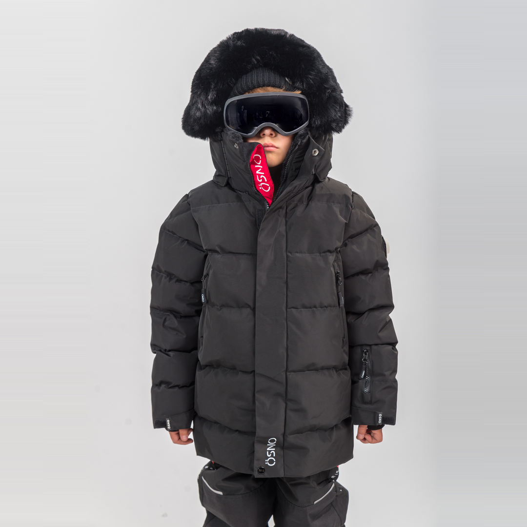 Child wearing a black winter coat with fur hood and goggles on a white background