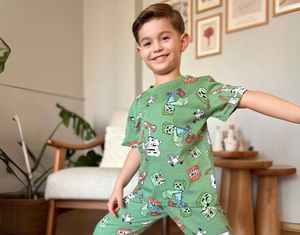 A young boy standing with his arms out in a green dinosaur-print pyjama set.