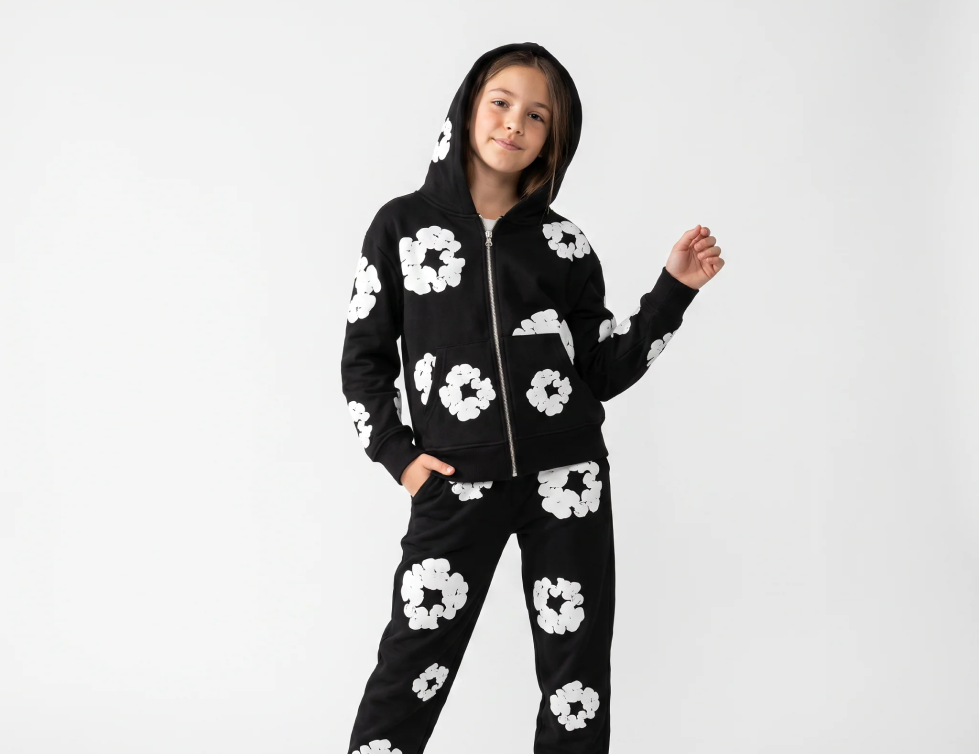 A girl in a black two-piece pyjama set with a white daisy print, hands tucked into her pockets.