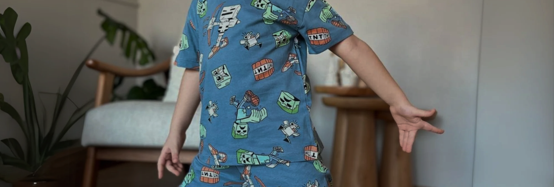 A boy in dinosaur-print pyjamas with his arms stretched out.