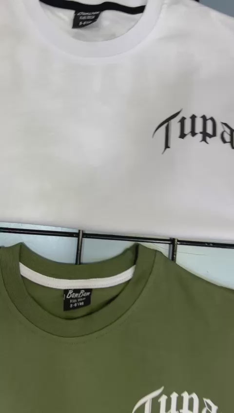 White and olive green T-shirts displayed on hangers, each featuring the word “Tupac” in bold black lettering, representing casual streetwear style.