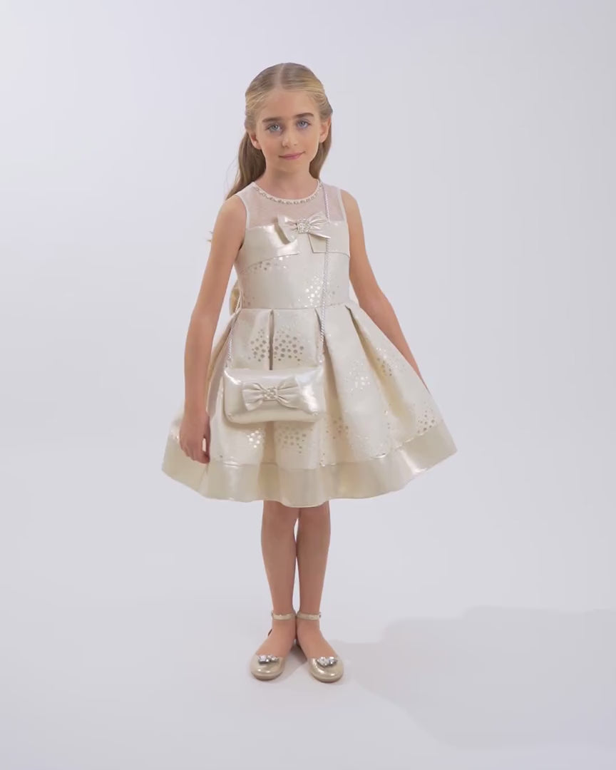 Girl in a sleeveless champagne-gold dress with pearl neckline, metallic sheen, and bow accents, posing elegantly in a minimalist white studio.